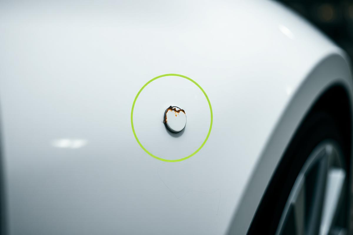 Close-up photograph of paint damage on a white vehicle panel, circled with a lime annotation